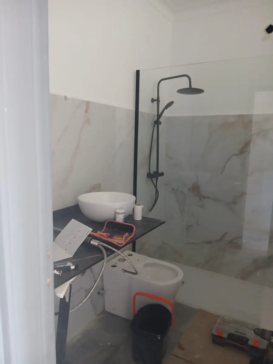 Bathroom under renovation with large marble-effect porcelain tiles, a frameless glass shower screen with black fittings and a countertop basin awaiting final installation