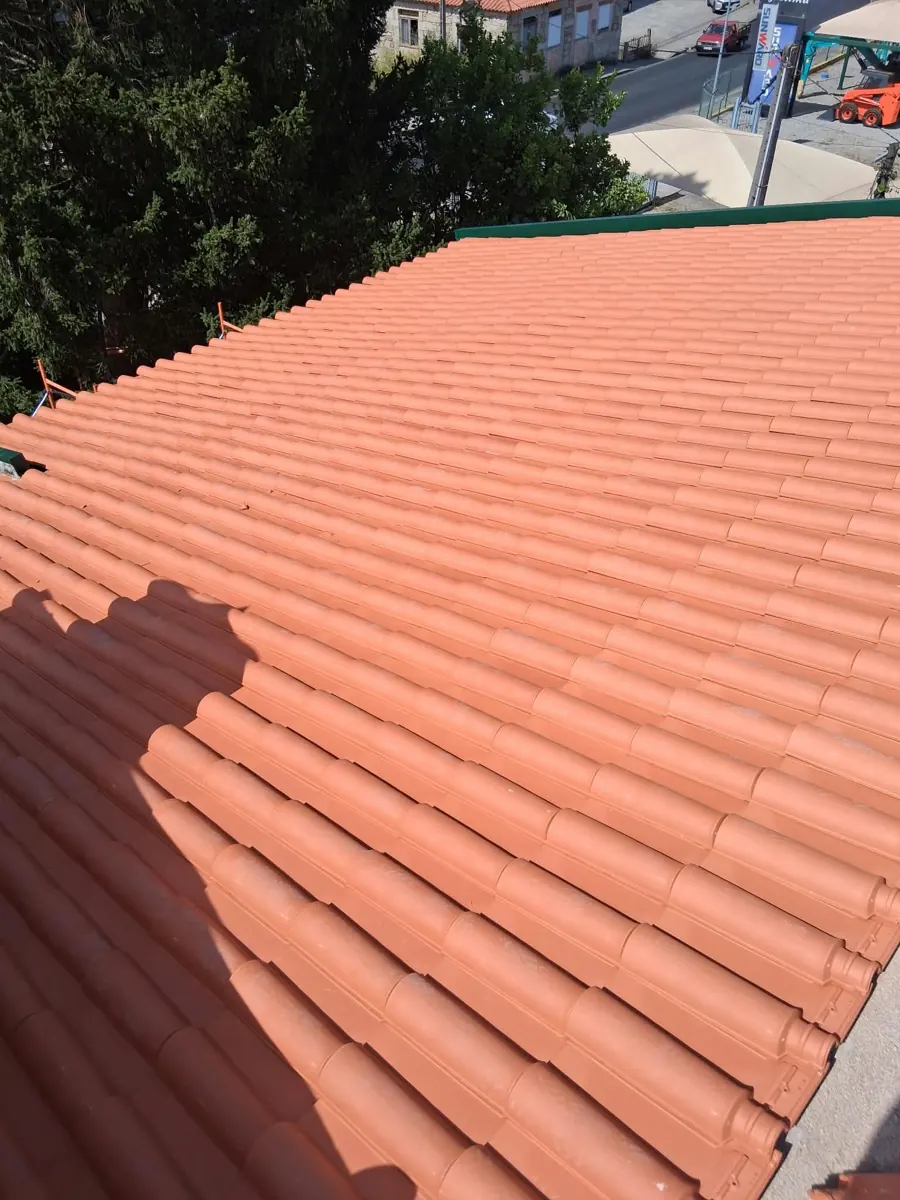 Close-up of a newly laid terracotta tile roof in Portugal with the tiles in even rows and a green ridge flashing along the top edge