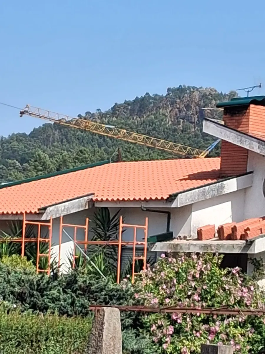 Villa roof in Portugal with new terracotta tiles on the main slope, orange scaffolding along the facade and stacked replacement tiles on the lower roof